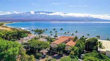 A coastal area with buildings, a parking lot, and a view of the ocean and mountains.