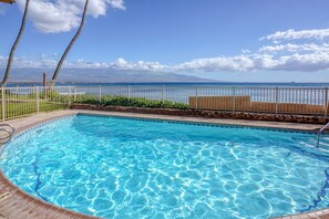 A clear blue swimming pool with a wooden deck, surrounded by a white fence and palm trees. - Suite Maui Paradise Condo (Wailuku)