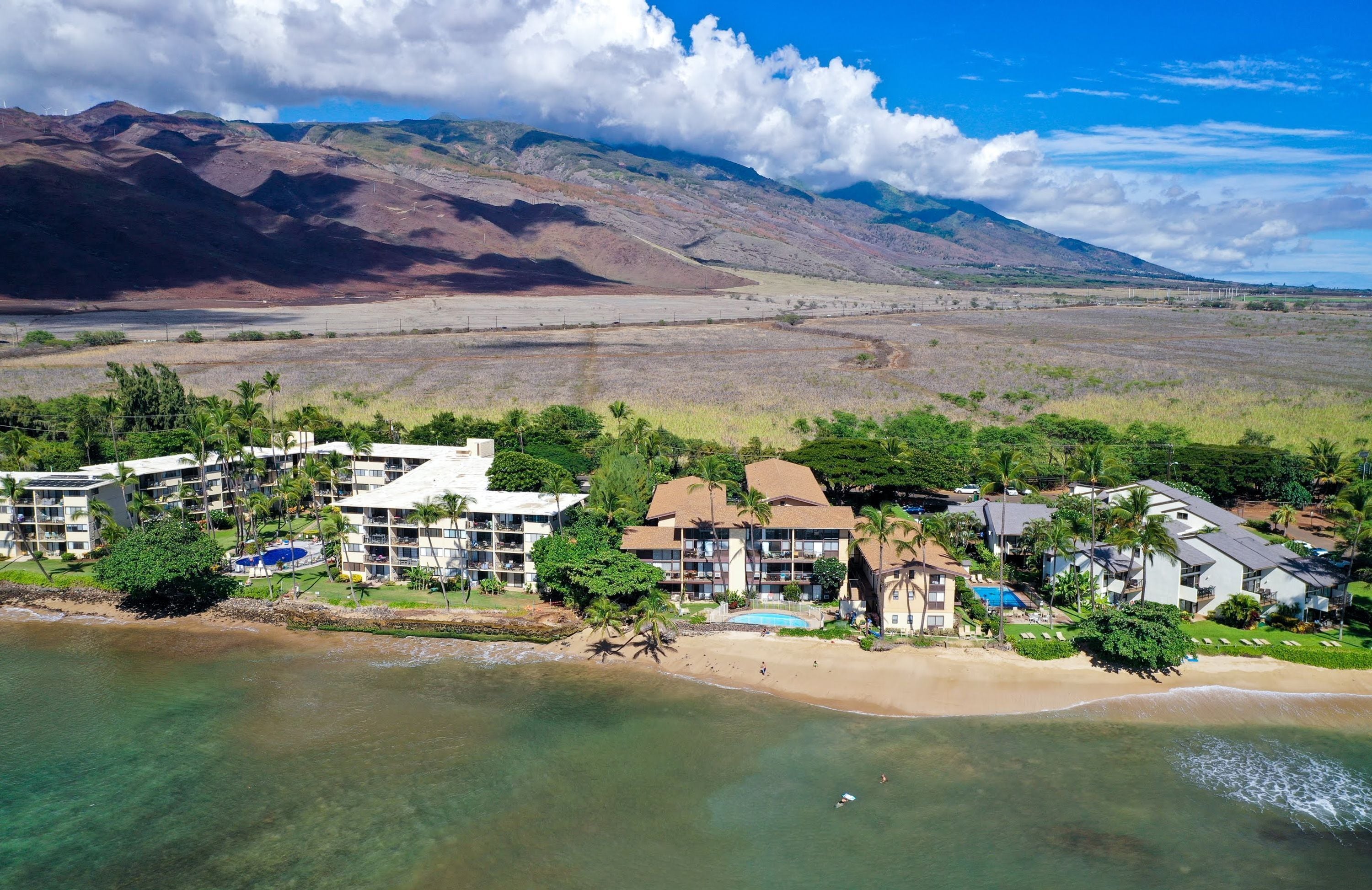 A coastal resort with multiple buildings, a beach, and mountains in the background.