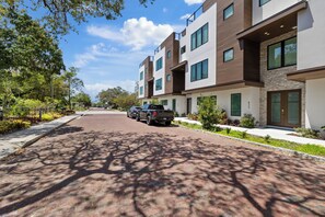 A modern multi-story residential building with a brick-paved driveway and a parked SUV.