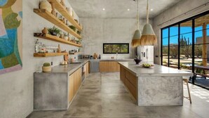 Una cocina moderna con una isla grande, repisas de madera y lámparas colgantes.
