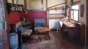 Une pièce rustique avec un plafond en bois, une carte accrochée au mur, une table en bois, un canapé à motifs et un petit bureau avec une lampe.