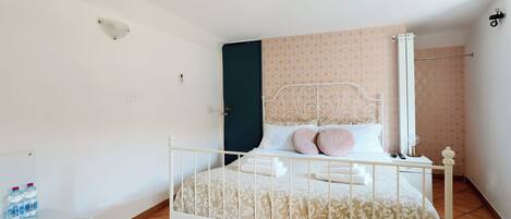 A bedroom with a bed, a white radiator, a water dispenser, and a door with a geometric-patterned curtain.