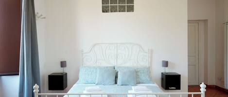 Una cama bien tendida con una colcha estampada, dos mesitas de noche con lámparas y una ventana con cortinas.