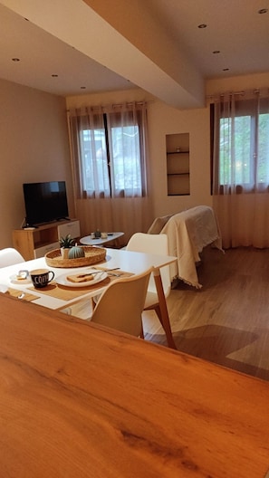 A cozy living room with a dining area, a television, and a large window with curtains.