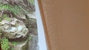 A view of a rocky landscape through a window with a curtain partially drawn. - Milies Creekside Studio (South Pelion)
