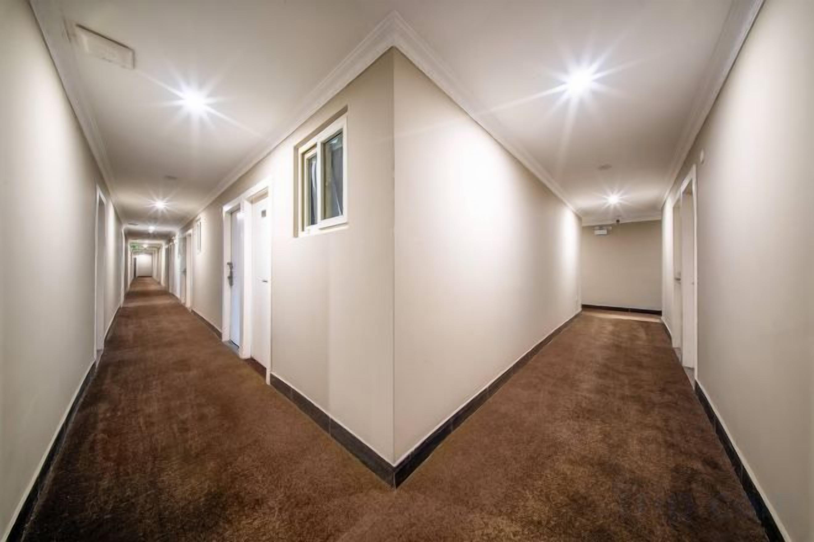 A long, narrow hallway with carpeted floors and white walls, leading to multiple doors.