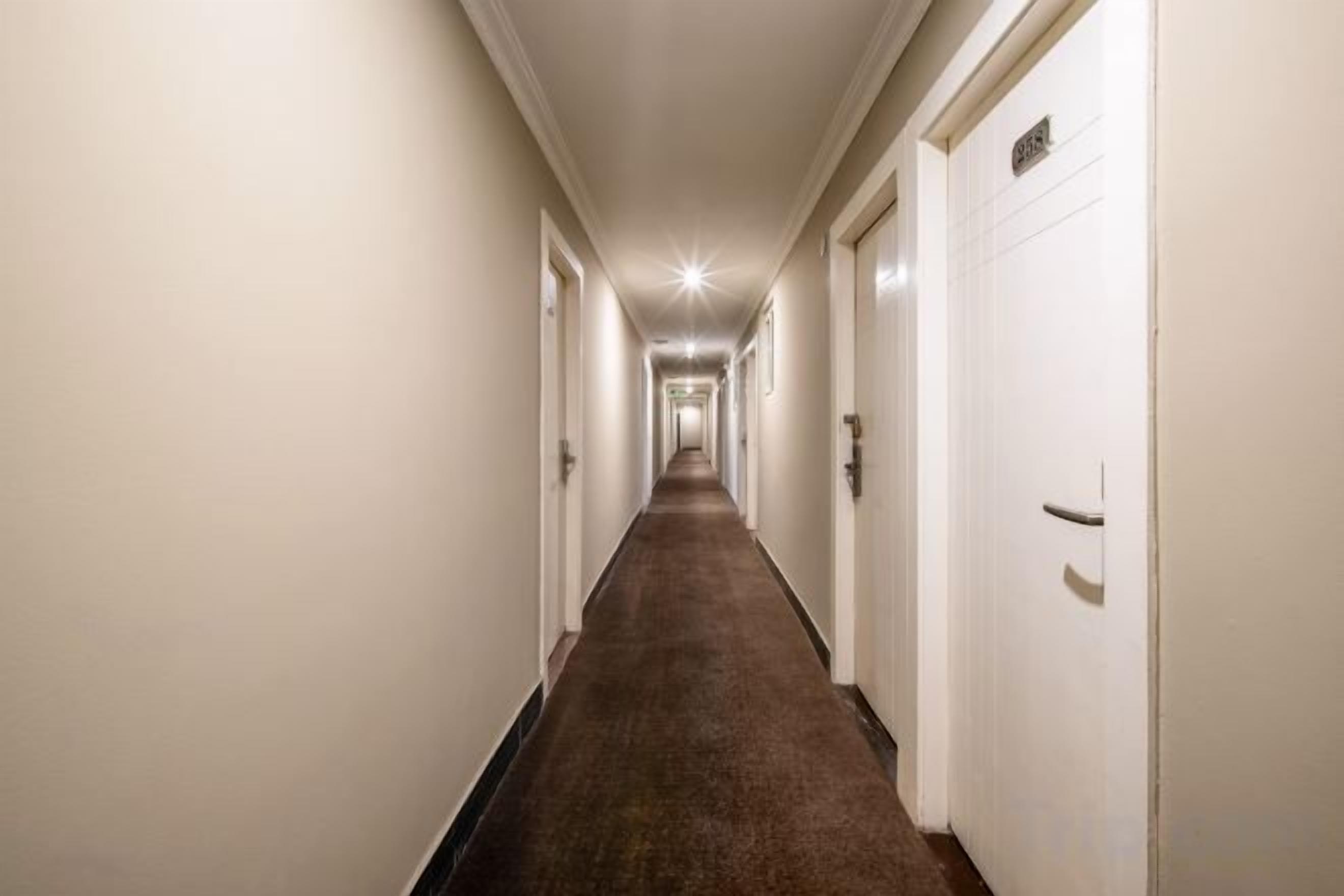 A long, narrow hotel corridor with doors on both sides, leading to individual rooms.