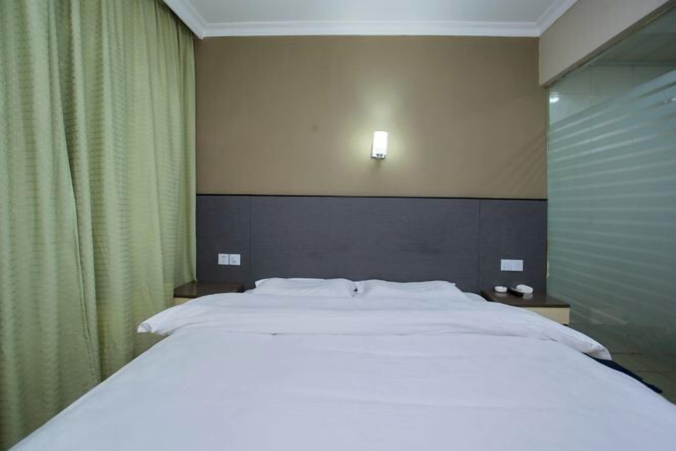 A hotel room with a bed, a nightstand, a wall-mounted light, and a window with a view.