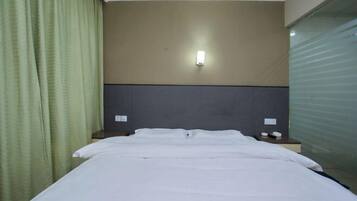A hotel room with a bed, a nightstand, a wall-mounted light, and a window with a view.