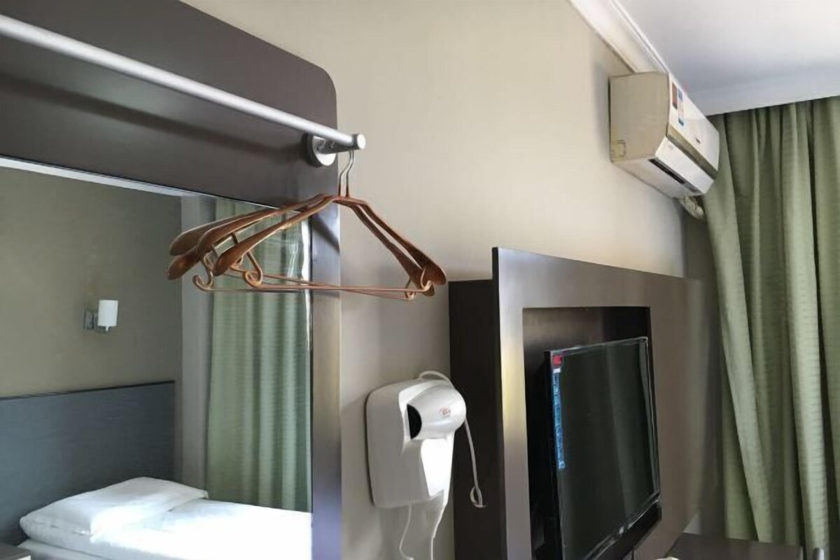 A hotel room with a bed, a TV, an air conditioning unit, a towel dispenser, and a coat rack.