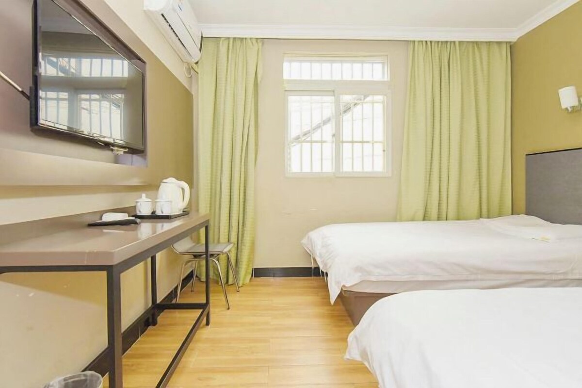 A hotel room with a bed, a desk with a chair, a television, and a window with curtains.