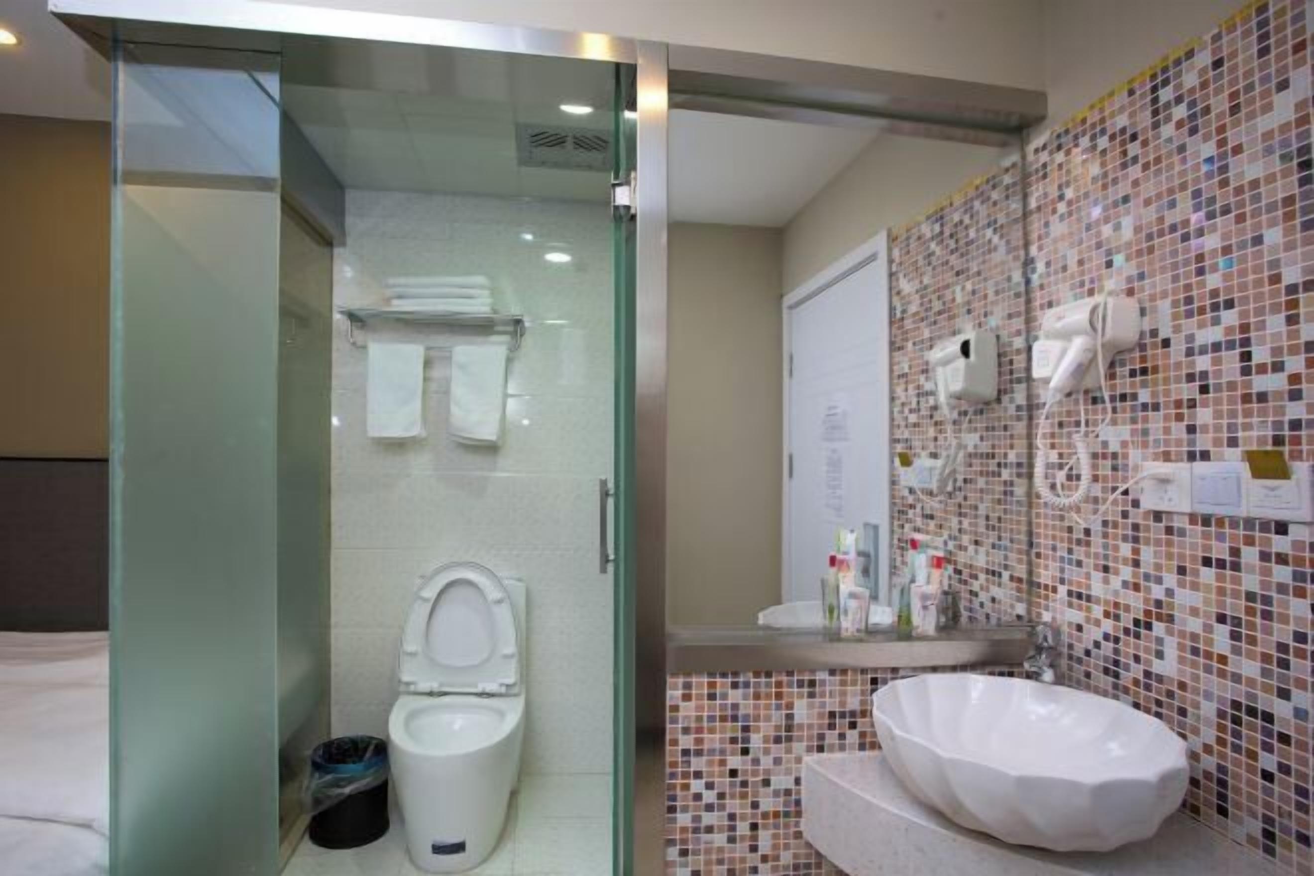 A modern bathroom with a glass-enclosed shower, a white toilet, a mosaic-tiled wall, and a large white sink.