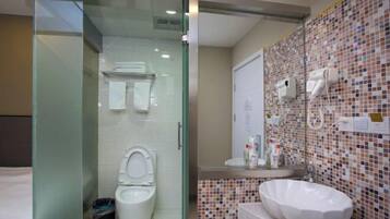 A modern bathroom with a glass-enclosed shower, a white toilet, a mosaic-tiled wall, and a large white sink.