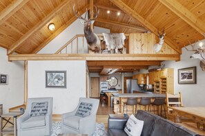 A spacious loft-style room with a high ceiling, wooden beams, and a mezzanine level.