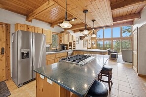 Une cuisine moderne dotée d’un îlot central, d’appareils électroménagers en acier inoxydable, de meubles de rangement en bois et d’une grande fenêtre offrant une vue sur l’extérieur.