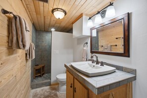 Ein Badezimmer mit Holzboden, einem weißen Waschbecken, einem Spiegel und einer Duschkabine.