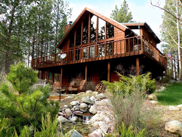Une cabane dotée d’une terrasse, entourée d’arbres et bordée d’un petit ruisseau.
