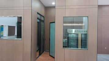 A hallway with a glass door, a wall-mounted refrigerator, and a trash bin.