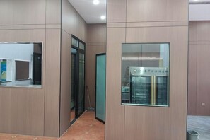 A hallway with a glass door, a wall-mounted refrigerator, and a trash bin.