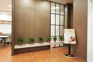 Zona de recepción con un banco, plantas en macetas y un cartel.