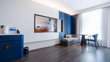 Une chambre d’hôtel moderne avec une grande fenêtre, un canapé, une petite table et un meuble bleu.