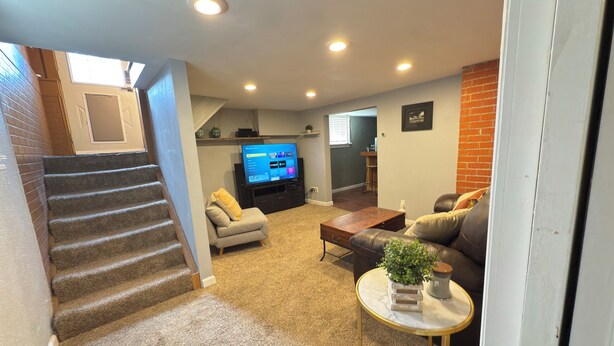 A living room with a staircase, a sofa, a coffee table, and a TV. - Cozy Craftsman Home Close to UW and Downtown (Laramie)