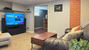 A living room with a flat-screen TV, a wooden coffee table, a leather sofa, and a brick accent wall. - Cozy Craftsman Home Close to UW and Downtown (Laramie)