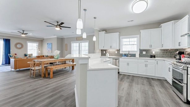 Una cocina moderna con armarios blancos, una isla central y un comedor con mesa de madera y bancos.