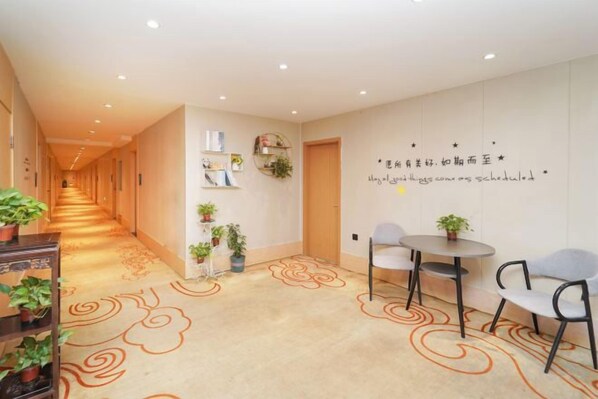 A hotel corridor with a carpeted floor, a seating area with chairs and a table, and a wall with decorative elements and text. - Xinzhuo Select Hotel (Shanghai)