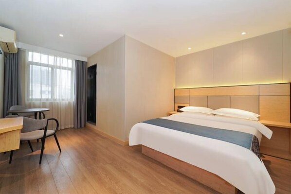 A modern hotel room with a wooden floor, a bed with white bedding, a desk with a chair, and a window with curtains.