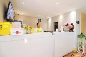 A hotel reception desk with a television, a digital screen, and various items like a yellow box, a white container, and a vase with flowers.