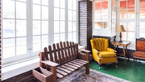 A room with large windows, a wooden bench, a yellow armchair, and a patterned rug.