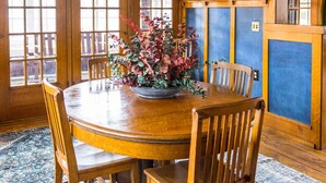 A dining room with a round wooden table, six wooden chairs, a floral centerpiece, and a large window with a view.