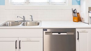 A modern kitchen with white cabinets, a stainless steel dishwasher, and a double sink.