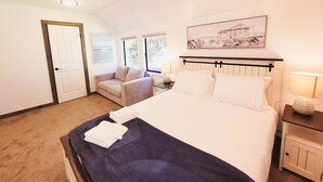 Un dormitorio con cama, mesita de noche, silla, puerta y ventana.