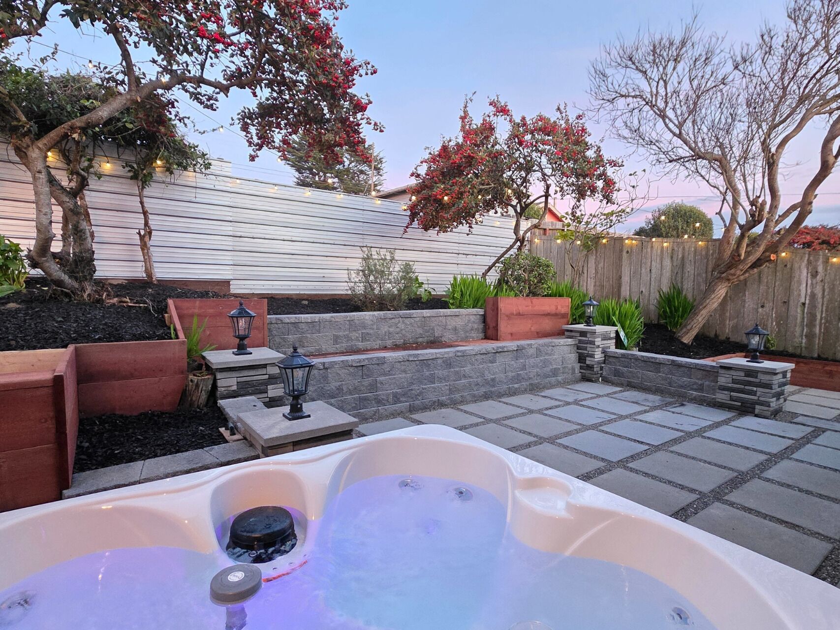 A backyard with a hot tub, stone steps, and a wooden fence.