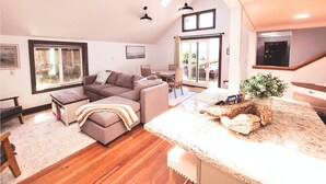 Amplia sala de estar con un ventanal, un sofá acogedor, una mesa de comedor y una cocina con mostrador y planta en maceta.