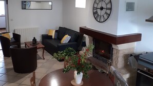 A living room with a fireplace, a round table with chairs, a sofa, and a large wall clock. - QUIETLY SITUATED VACATION HOME (Azerables)