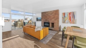 Een moderne woonkamer met een bank, een open haard, een eettafel en uitzicht op de stad.