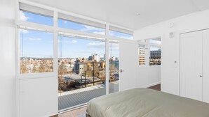 Een slaapkamer met een groot raam, een bed en uitzicht op een stadsgezicht.