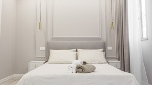 A neatly made bed with pillows and a rolled towel, a bedside table, and a wall-mounted light fixture.