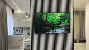 A modern interior with a large flat-screen TV mounted on a black and white striped wall, a marble-tiled floor, and a dining area with a white table and chairs.