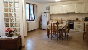 Una cocina con armarios blancos, un refrigerador, una estufa y un comedor con sillas y una mesa de madera.