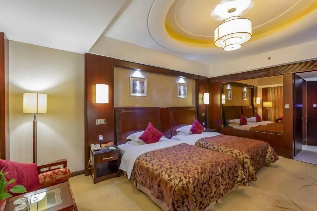Una habitación de hotel con dos camas, un escritorio, una lámpara y un espejo.