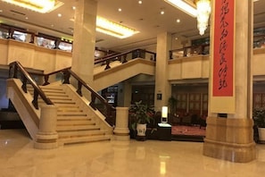 Un hall d’hôtel doté d’un grand escalier, de plusieurs étages et d’une grande banderole rouge.