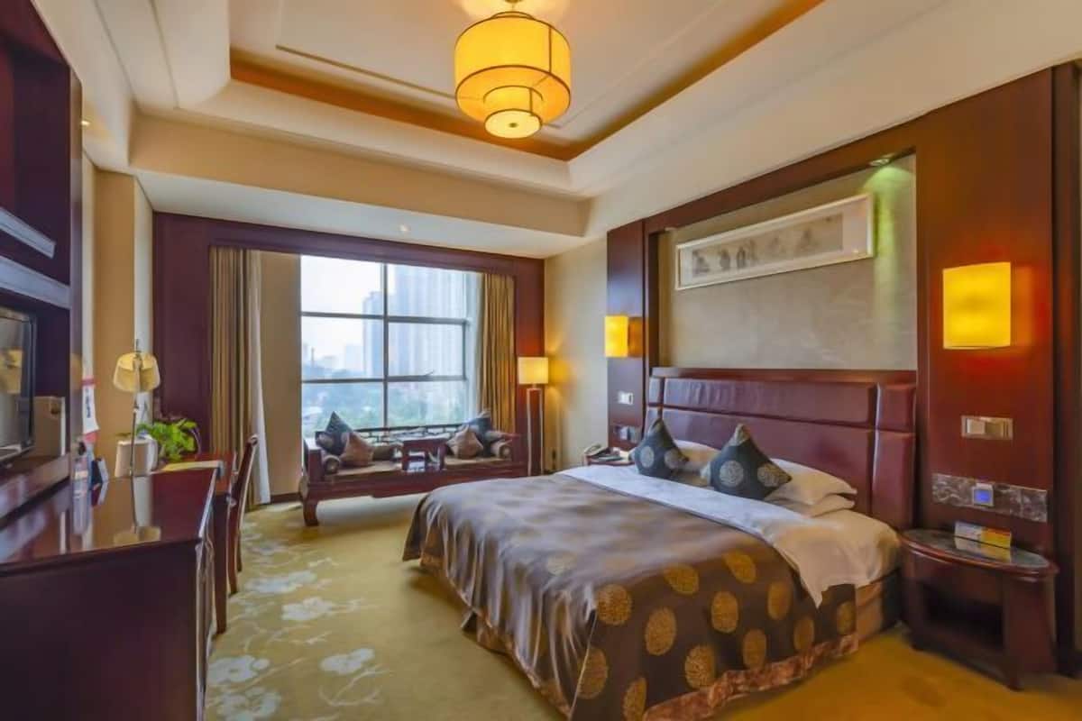 Habitación de hotel con una cama grande, un escritorio, una silla, un sofá y una ventana con vistas a la ciudad.