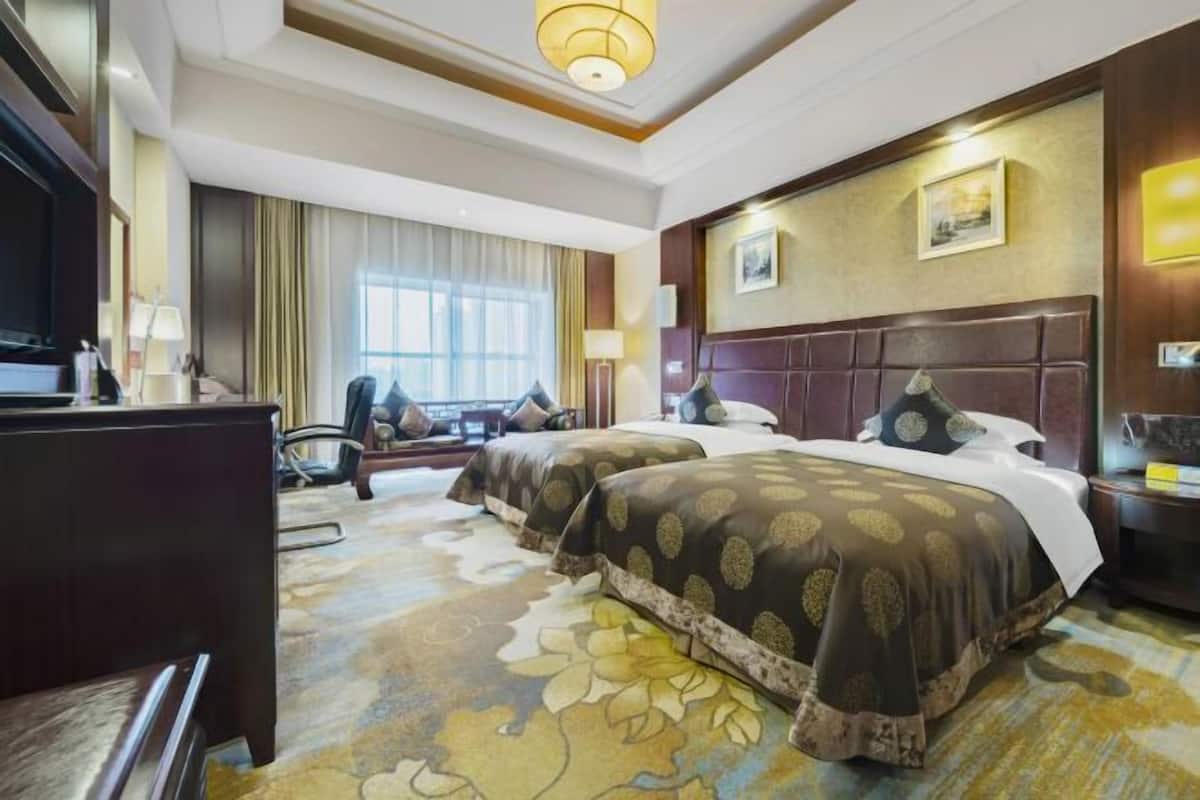 Una habitación de hotel con dos camas, un escritorio, una silla, un televisor y un ventanal grande.