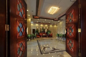 Eine Lobby mit poliertem Marmorboden, einem Empfangstresen und traditionellen Holztüren mit aufwendigen Verzierungen.