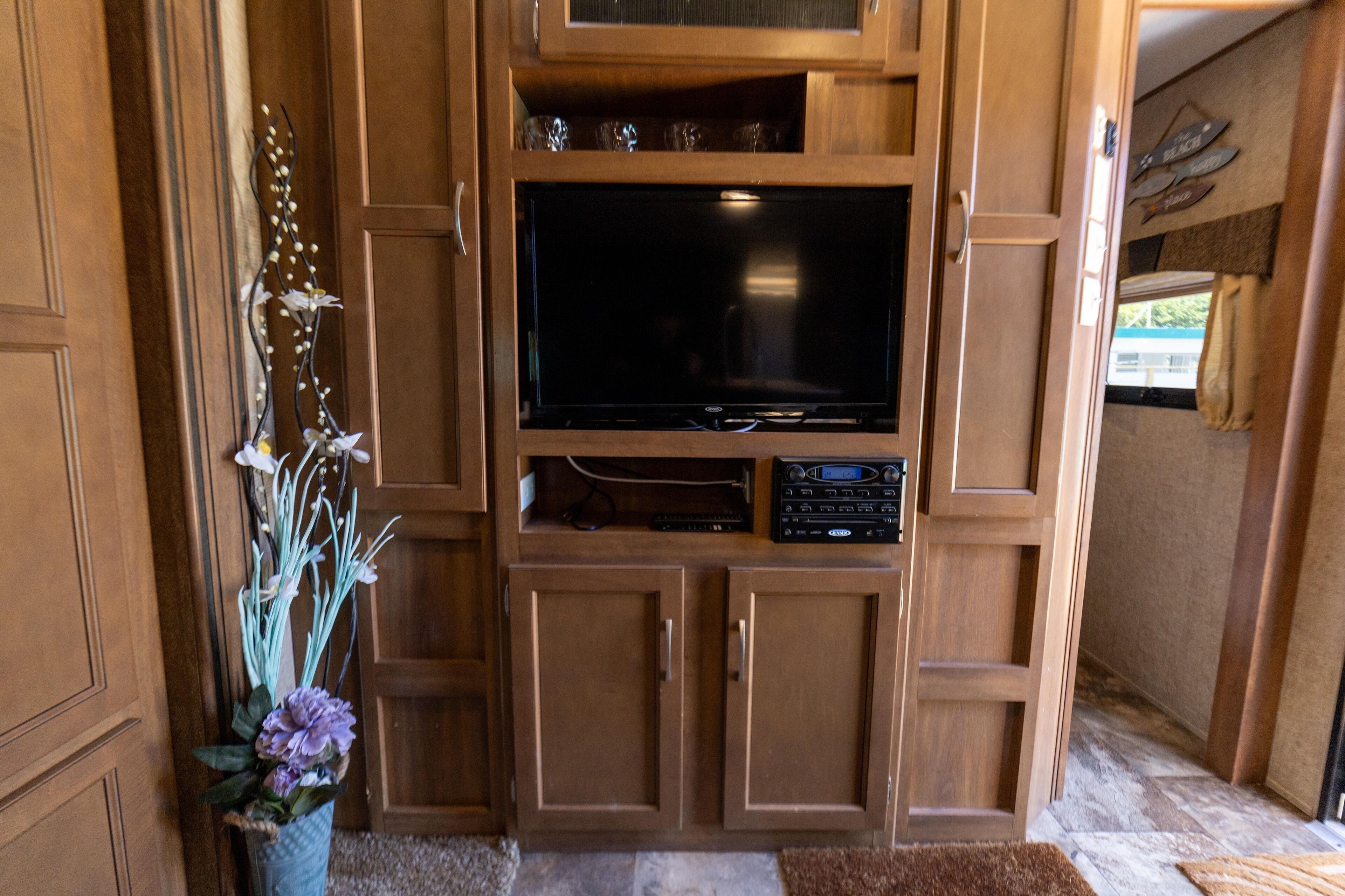 Un meuble de rangement en bois pour appareils multimédias, comprenant un téléviseur à écran plat, un système audio et des objets décoratifs.